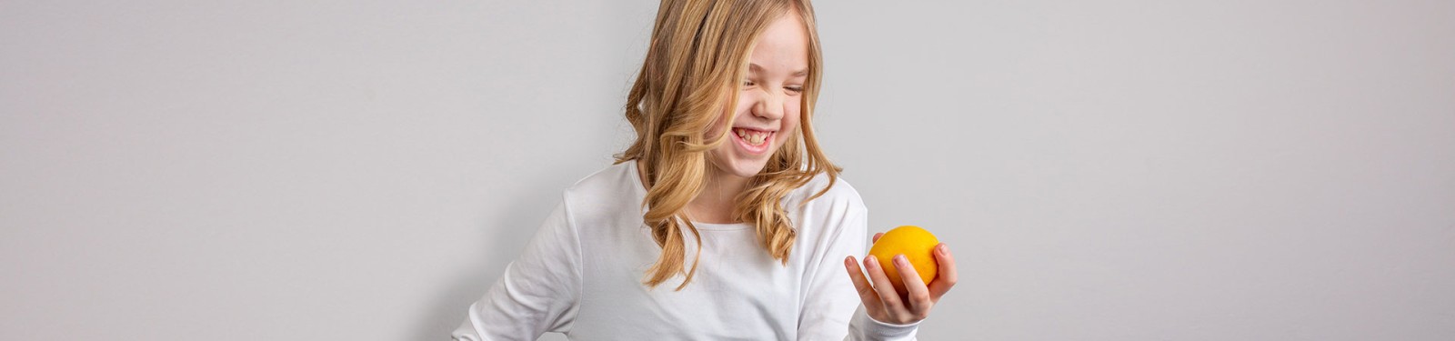 Kinderseite Ein Mädchen blickt auf ein Stück Obst in ihrer Hand und lacht.