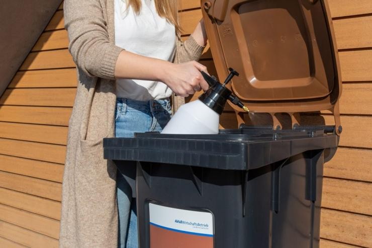 Biotonne innen besprühen Eine Frau besprüht das Innere einer Biotonne