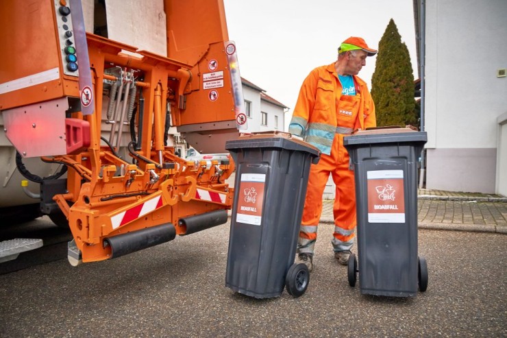 Ein Müllwerker zieht zwei Biomülltonnen, nebendran steht ein Müllfahrzeug
