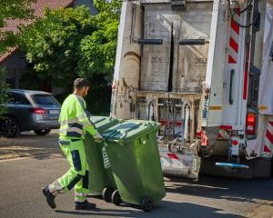 Ein Müllwerker schiebt zwei Abfalltonnen zum Müllwerkerfahrzeug