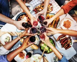 Grillgut auf einem Tisch, Menschen halten Gläser darüber und stoßen an