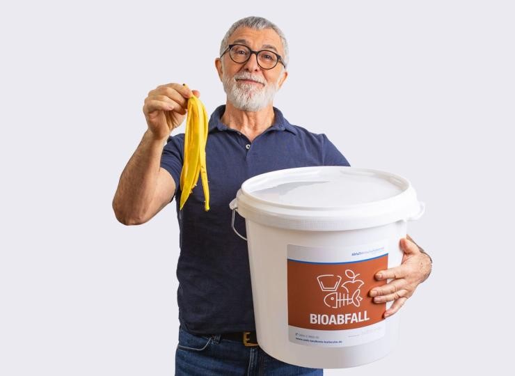 Ein Mann hält eine Bananenschale in der Hand und einen Eimer im Arm Ein Mann hält eine Bananenschale in der Hand und einen Eimer im Arm