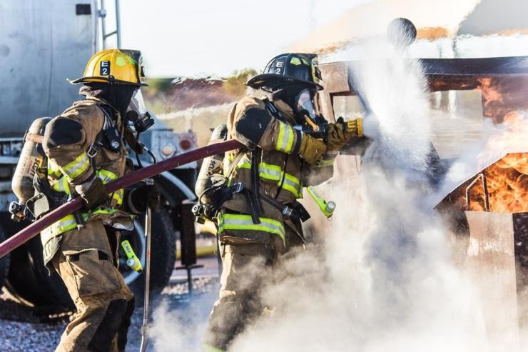 Zwei Feuerwehrleute löschen am hellichten Tag auf einem Platz ein Feuer