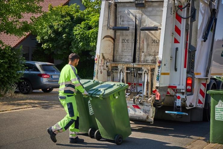 Ein Müllwerker schiebt zwei Abfalltonnen zum Müllwerkerfahrzeug