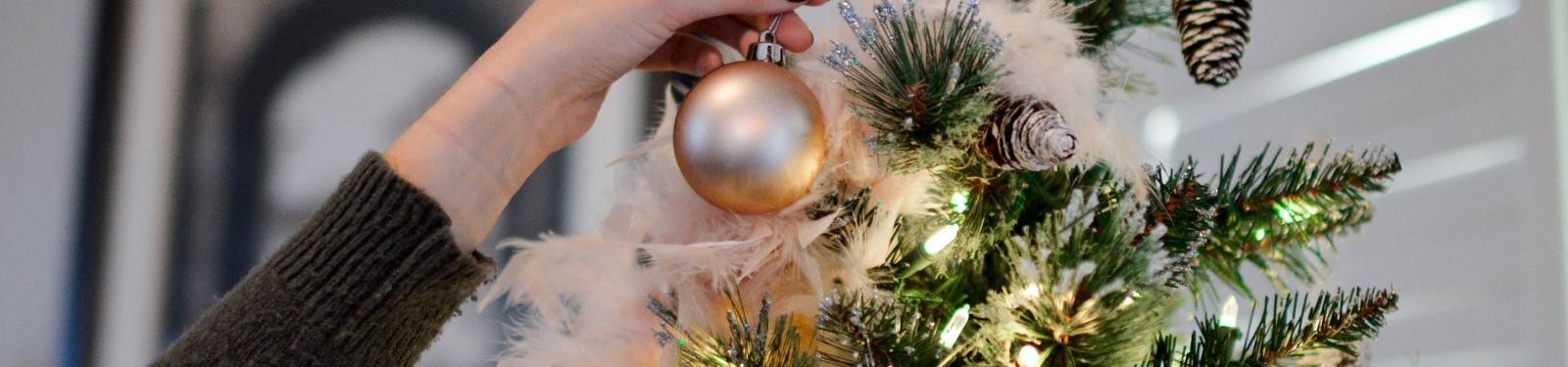 Eine Frau hängt eine Kugel an einen Weihnachtsbaumn Eine Frau hängt eine Kugel an einen Weihnachtsbaumn