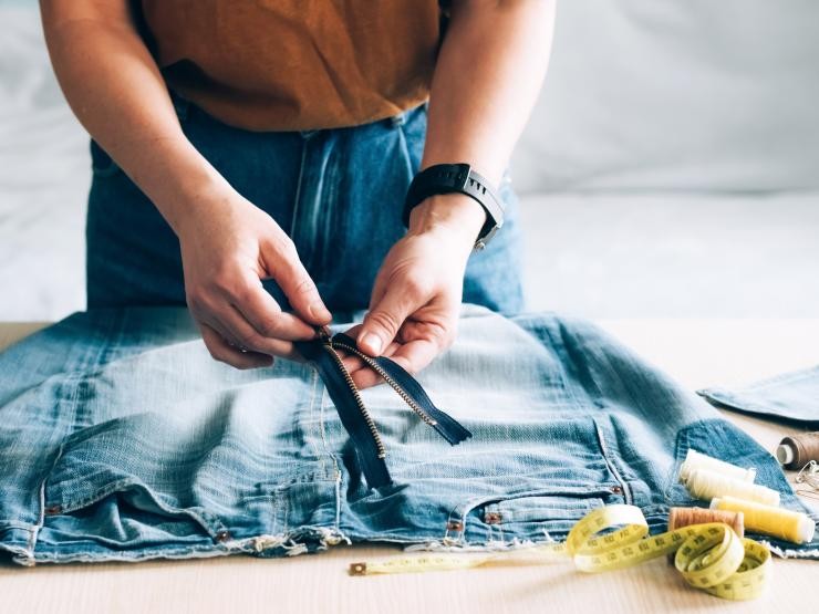 Eine Person repariert den Reißverschluss einer Jeanshose Eine Person repariert eine Jeanshose