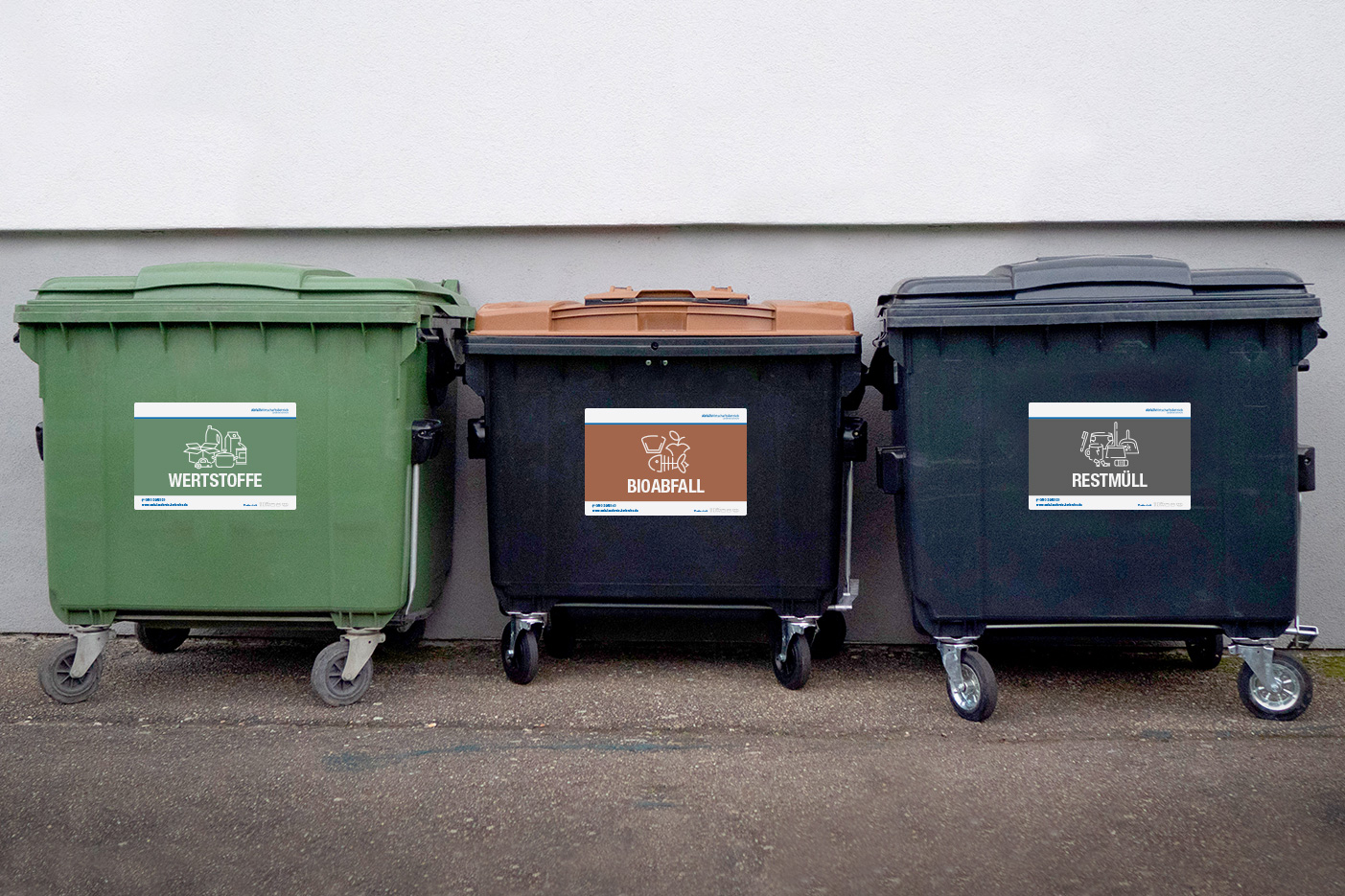 Abfallbehälter mit Tonnenaufklebern vor einer weißen Wand.