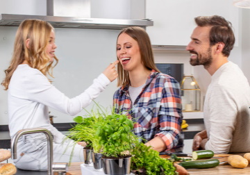 Privatkunden Eine Familie steht in der Küche; das Mädchen sitzt auf der Küchenzeile und reicht