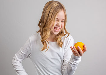 Ein Mädchen blickt auf ein Stück Obst in ihrer Hand und lacht.