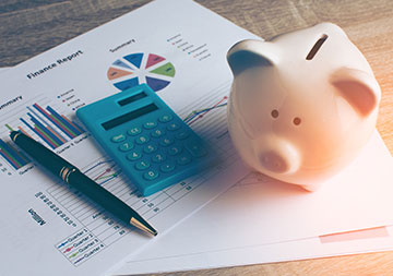 Ein Sparschwein, Taschenrechner und Kugelschreiber sind auf einigen Unterlagen platziert.