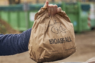 Eine Männerhand hält einen gefüllten Papierbeutel für Bioabfall in die Höhe
