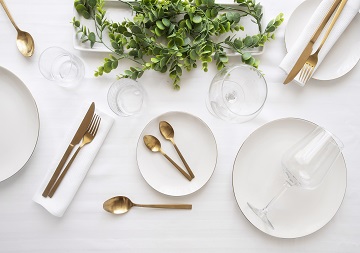 Ein feierlich, mit weißen Tellern und goldenen Besteck, und Gläsern gedeckter Tisch