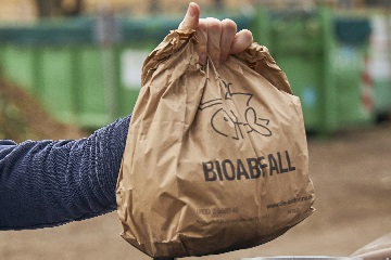 Eine Männerhand hält einen gefüllten Papierbeutel für Bioabfall in die Höhe