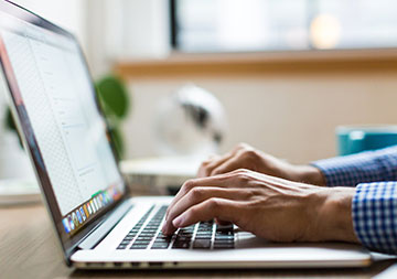 Zwei Hände tippen etwas in einen geöffneten Laptop ein