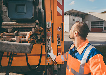 Gewerbeabfall entsorgen Ein Müllwerker bedient das Müllfahrzeug; die Tonne wird entleert.